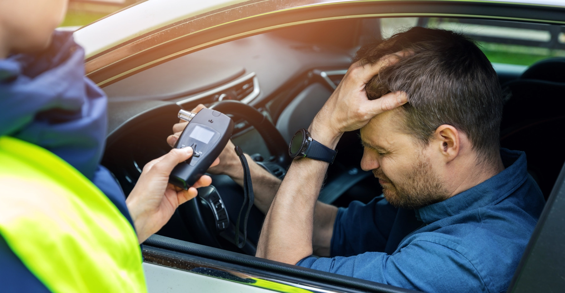 man in his car with a police officer holding a breathalyzer