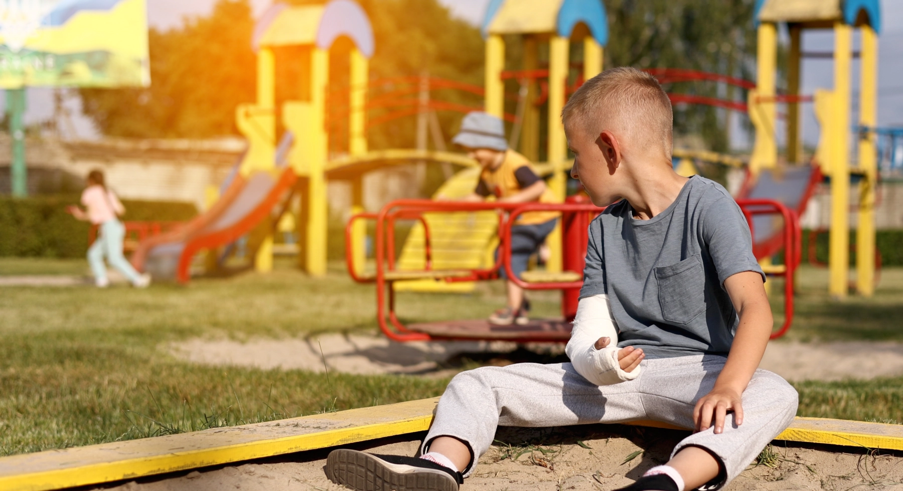 A Kid sitting in a playground with a cast on their arm