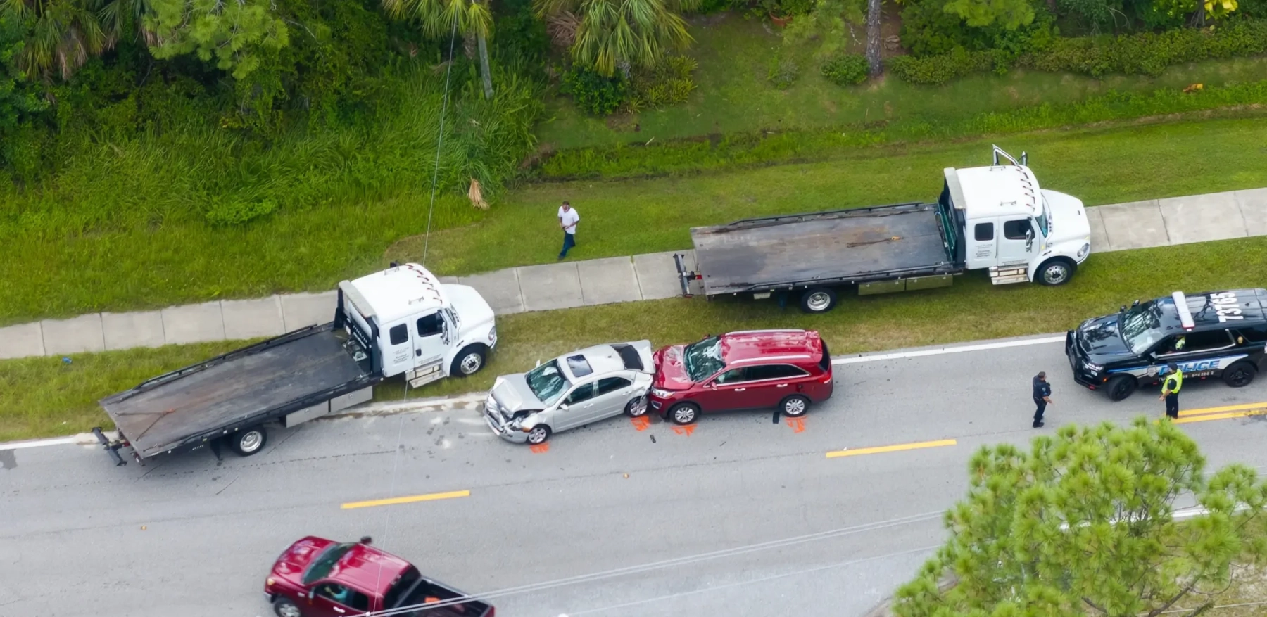 two tow trucks parked next to a rear-end car crash scene